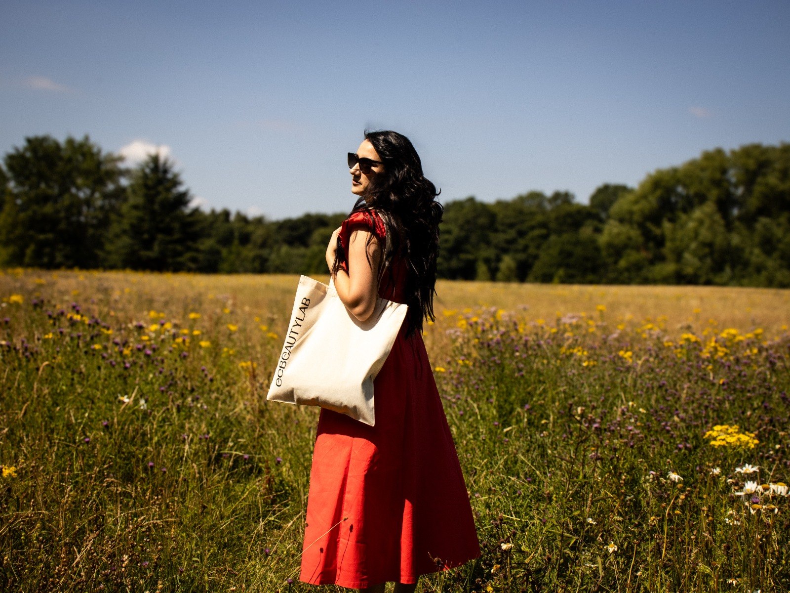 Eliz Chausheva, founder of ECBEAUTYLAB, in a wildflower meadow with an ECBEAUTYLAB tote bag